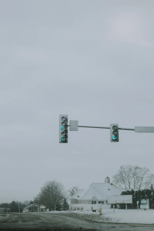 a green street light in the snow by a house