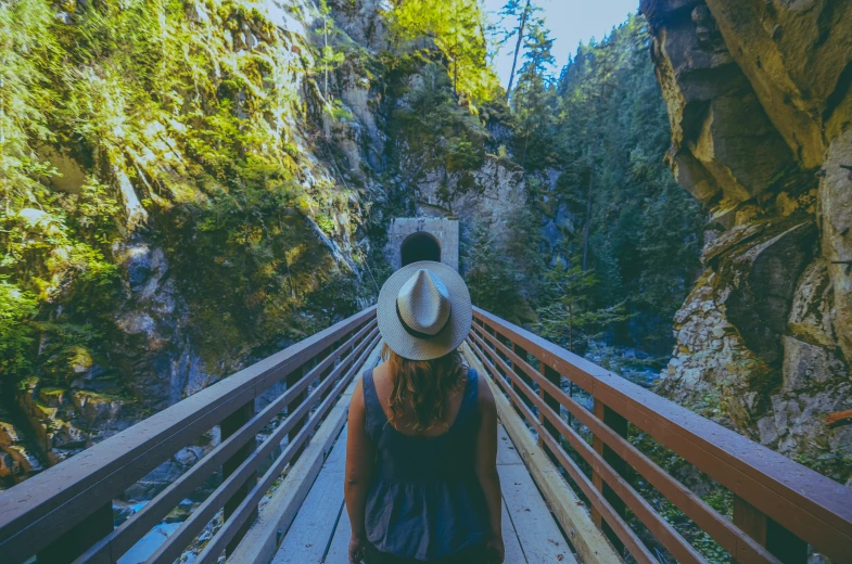 a person with a hat and a jacket walking on a wooden platform between two large cliffs