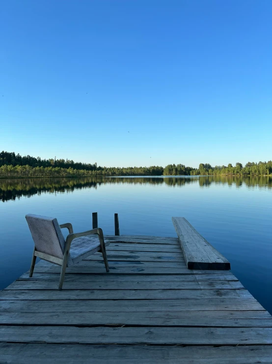 a small wooden dock in a lake on which two lawn chairs sit