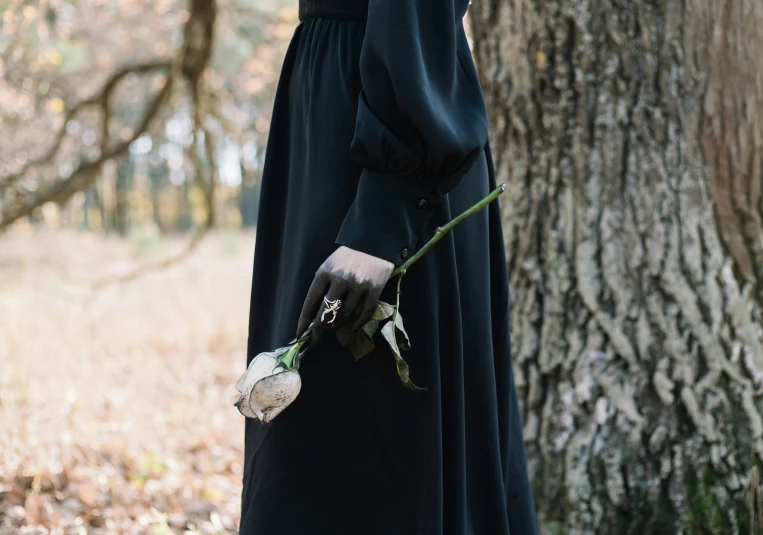 a woman standing in the woods with her hand over her face and wearing black gloves