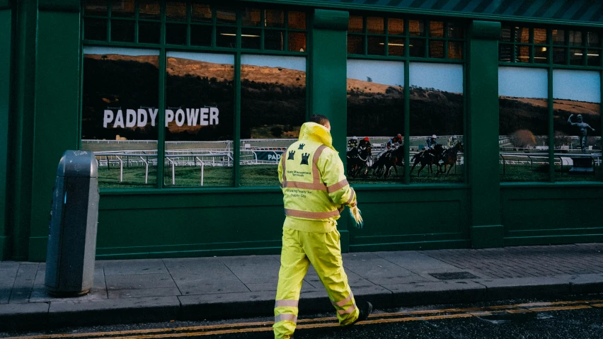 a man wearing a neon yellow outfit walks past a horse race store