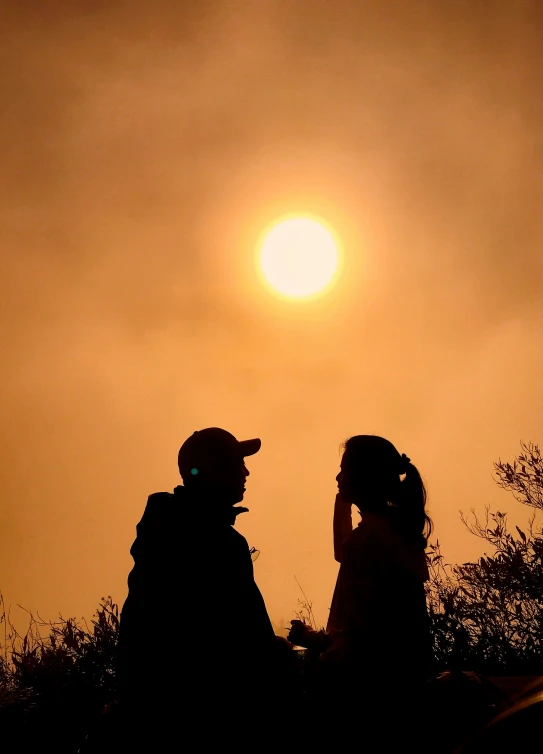 a couple standing side by side in front of the sun