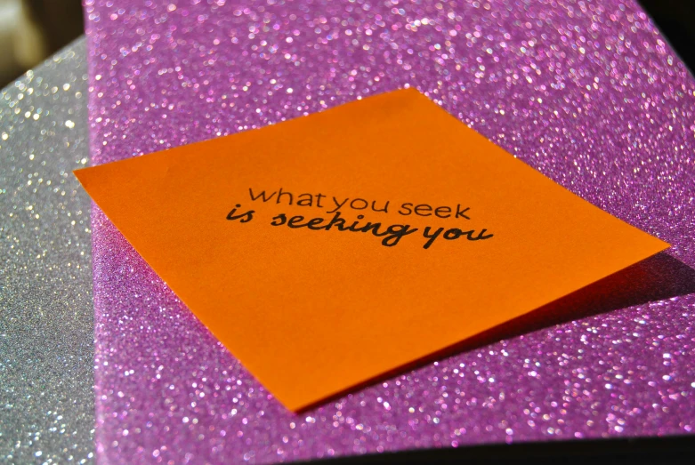 an orange piece of paper on top of purple glitter with a note