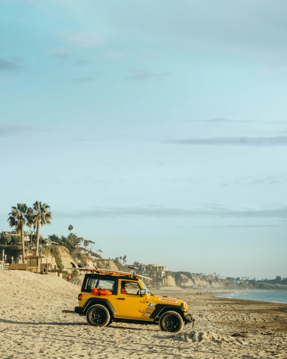 a yellow jeep driving on the sand by water