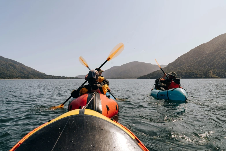 two kayakers paddling in water with mountains in the background