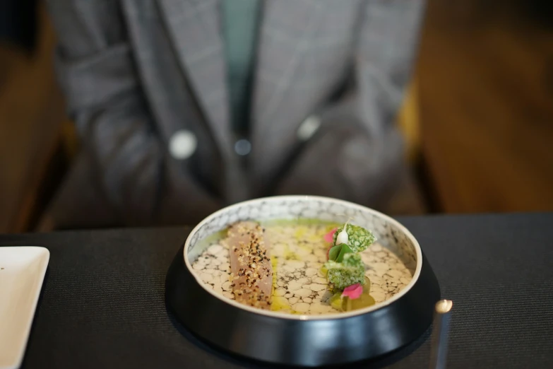 a black and white tray a man in a gray jacket and a small bowl of food