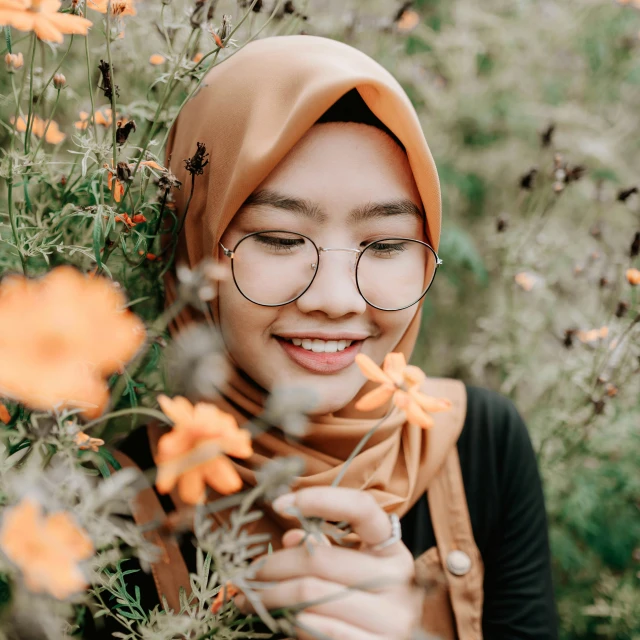 young woman wearing glasses smiles while surrounded by orange flowers