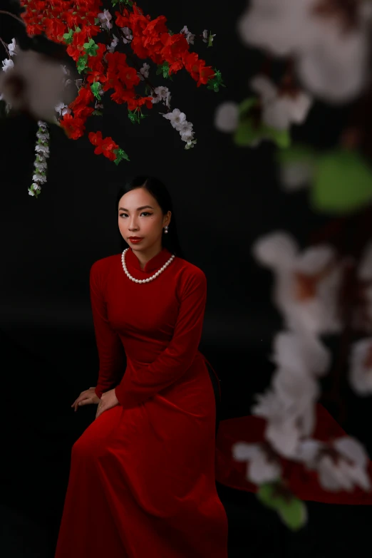 a woman in a long red dress stands under a cherry blossomy tree