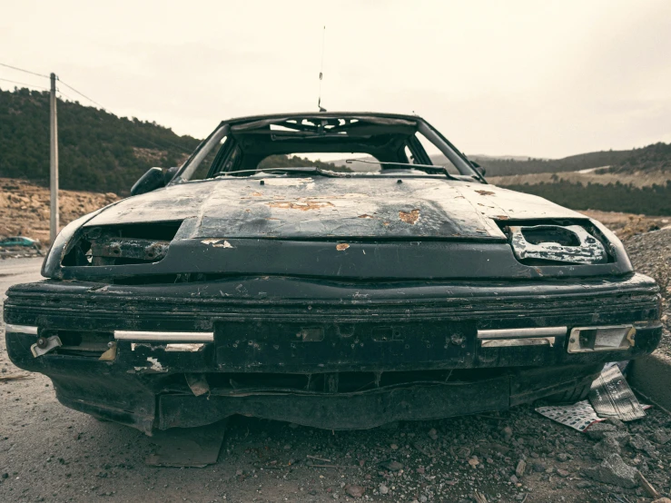 a rusty car parked on a road next to a hill