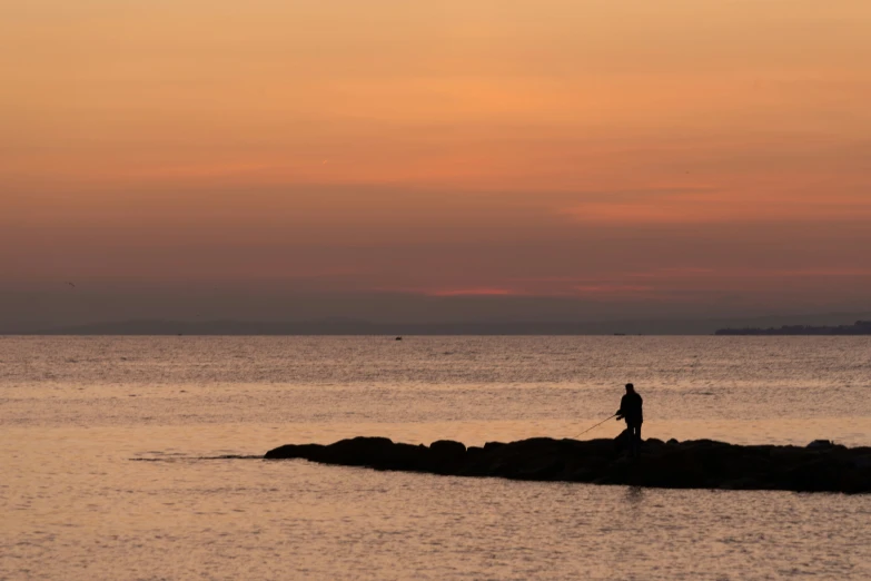 a person on the shore at sunset by water