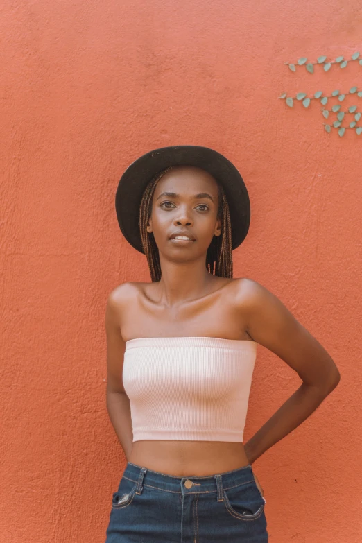 a woman in a black hat and denim skirt standing against a wall