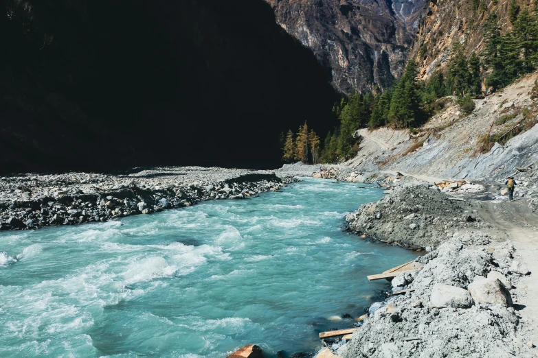 people walk along a rocky and blue river in mountains