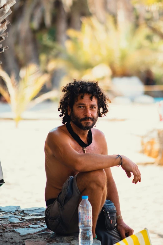 there is a man with long hair sitting with a surfboard