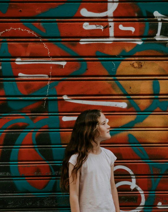 a girl standing against a wall with graffiti
