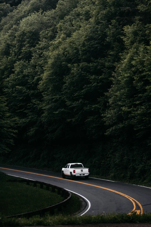 the white truck is driving along a curved road with trees in the background