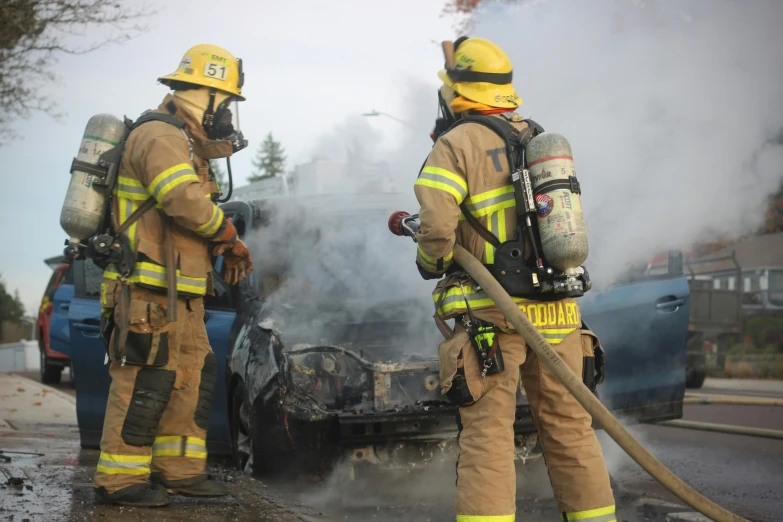 two firefighters standing by a burnt car in the street