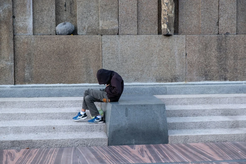 a man sits on the curb beside a concrete cube while holding his head