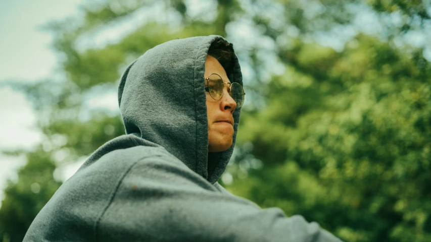 man in hoodie gazing away with trees and sky behind