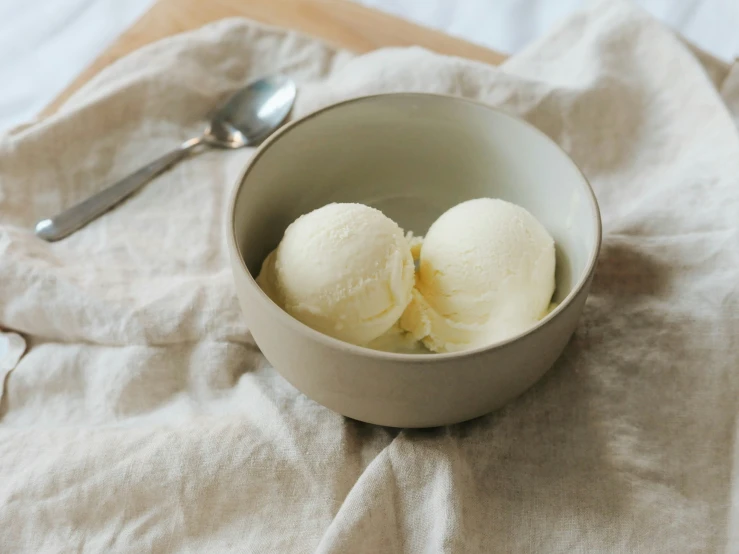two scoops of ice cream in a bowl on a cloth with a spoon