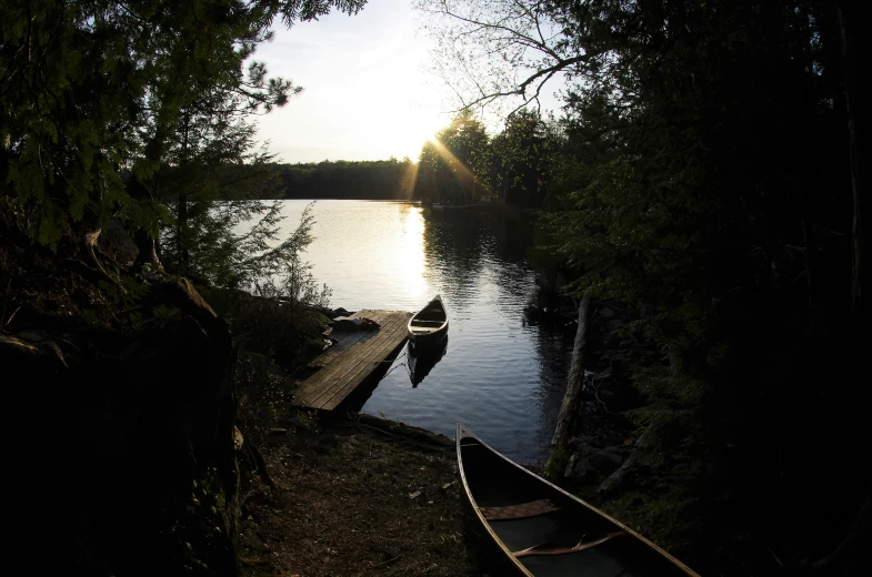 the sun is setting over a lake with canoes tied up to it