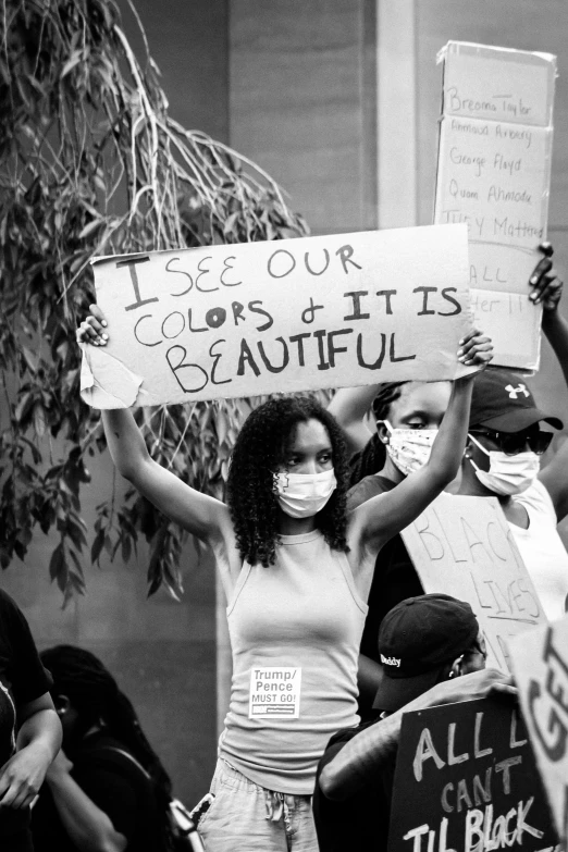 a woman in a  and a face mask holds signs while surrounded by people