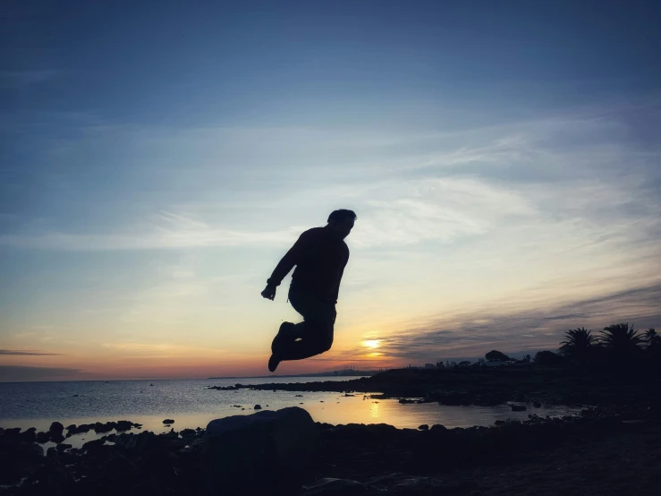 a silhouetted person jumps into the air while looking at the water