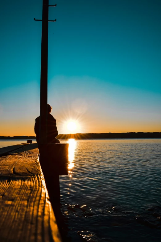 a person sitting on a bench watching the sun go down over the ocean