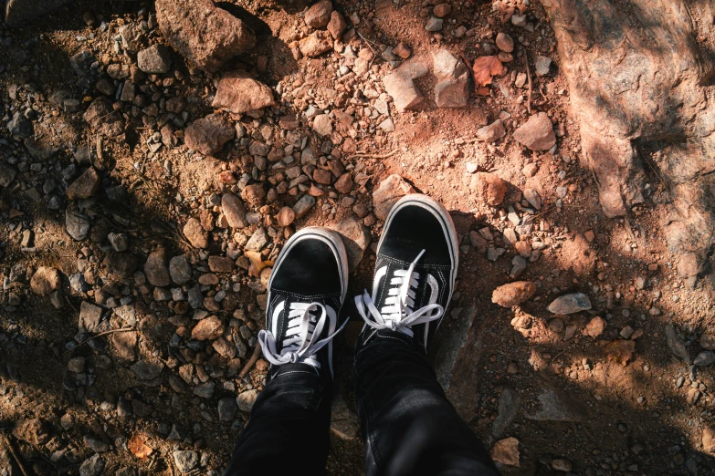 a person with shoes standing next to rocks on a rock - strewn ground