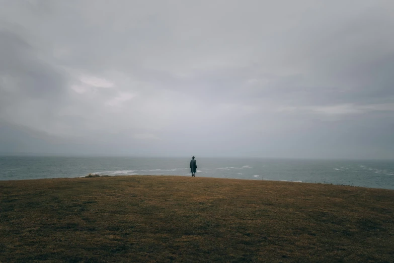 the man stands on a hill looking out into the ocean