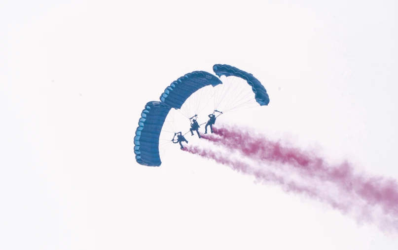 the smoke trail from an aeroplane is caught behind some parachutes