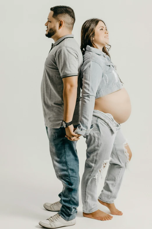 an pregnant couple hold their hands while standing against a backdrop