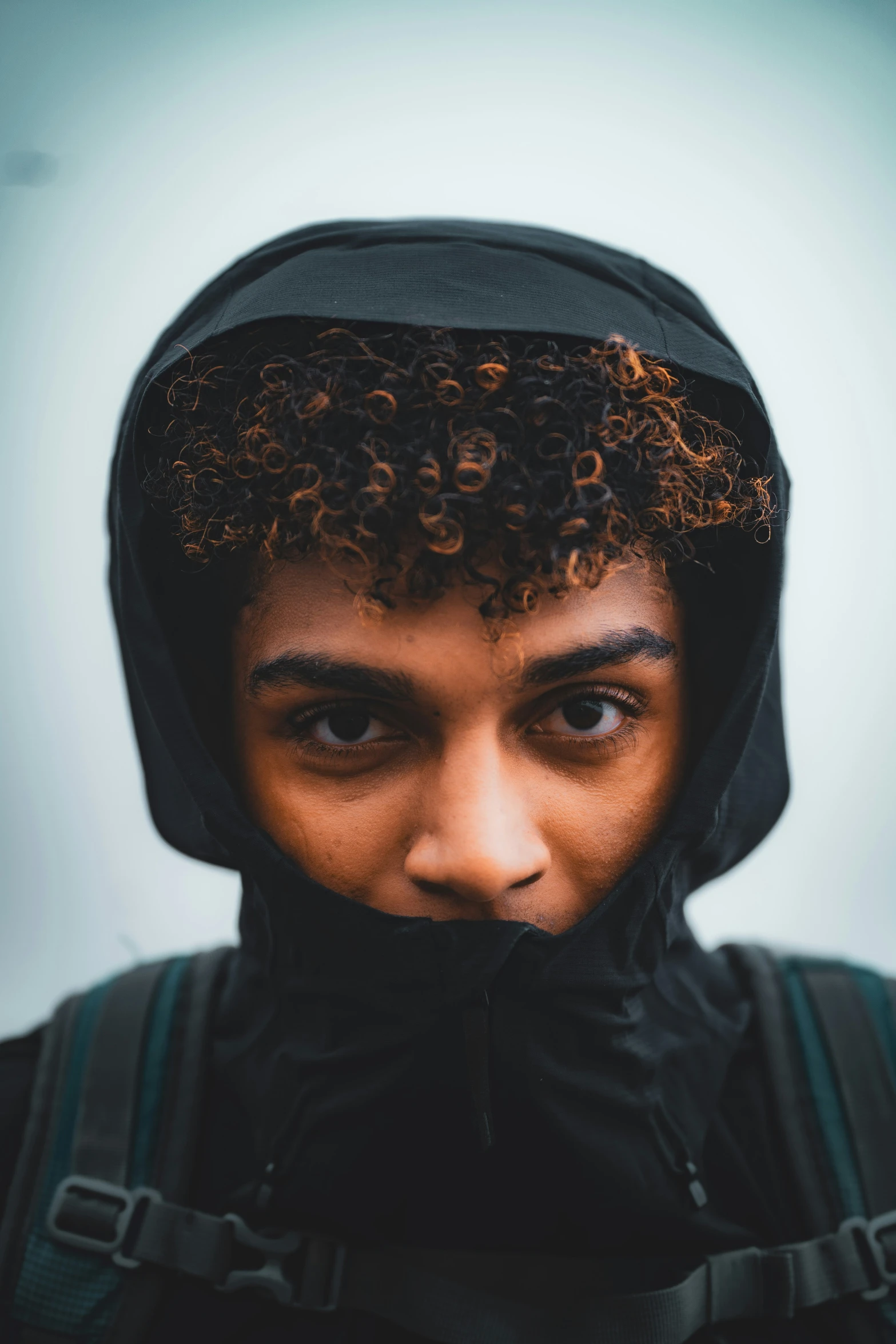 a young man with curly hair wearing a backpack