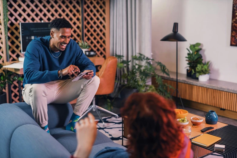 a young person smiles as he sits on a couch while another person talks with him