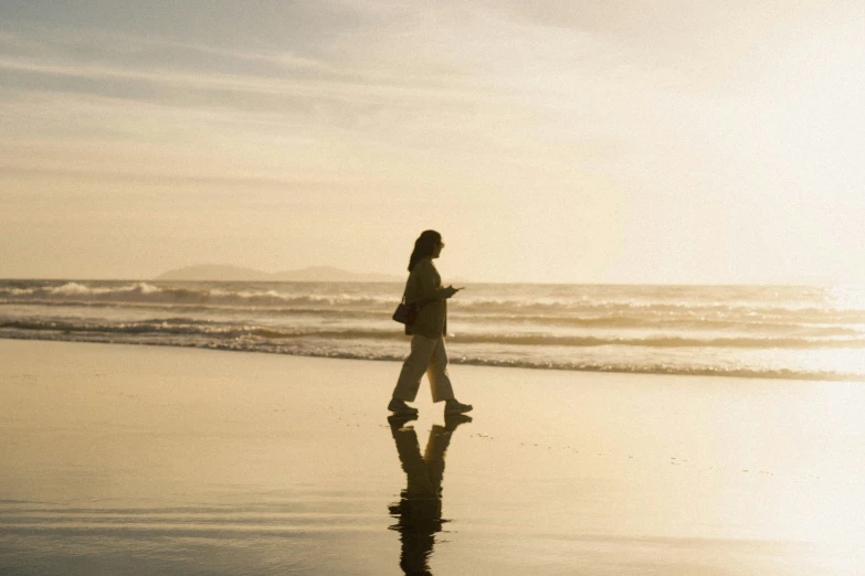 the woman is walking on the beach looking at her cell phone