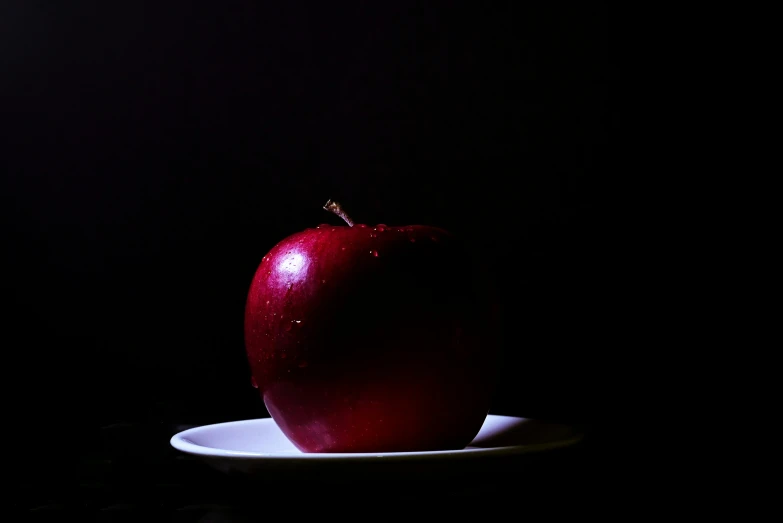 a single red apple sitting on a white plate