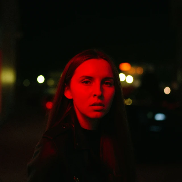 a person standing alone at night with car lights behind her