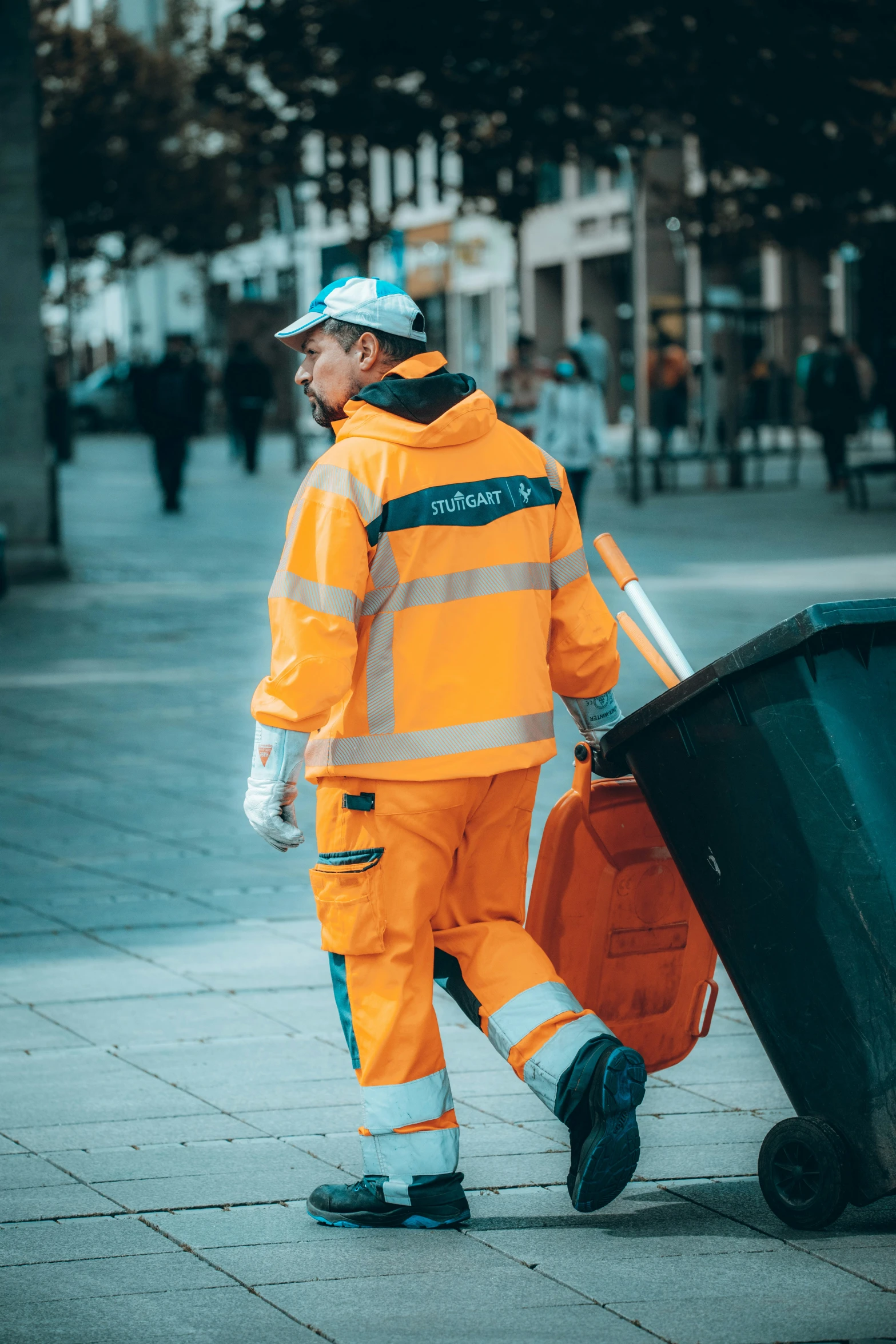 a man in safety gear hing a barrel next to a garbage can