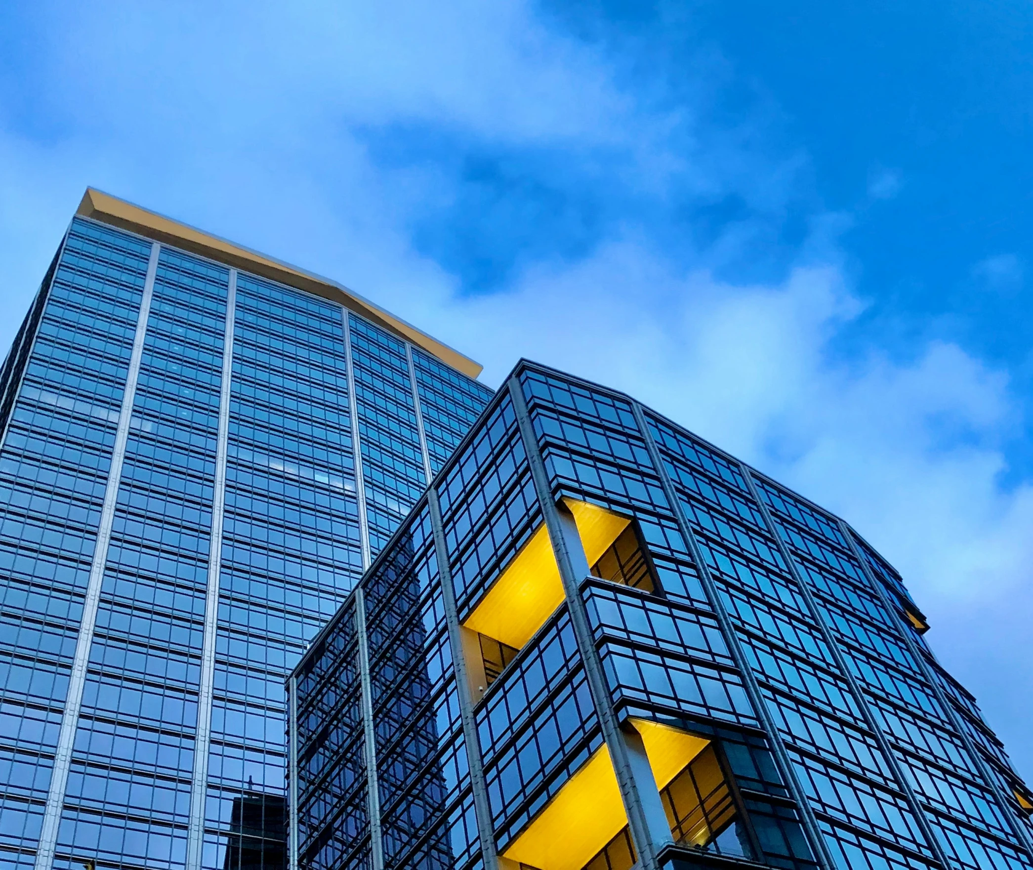 two buildings that have some glass and yellow lights on them