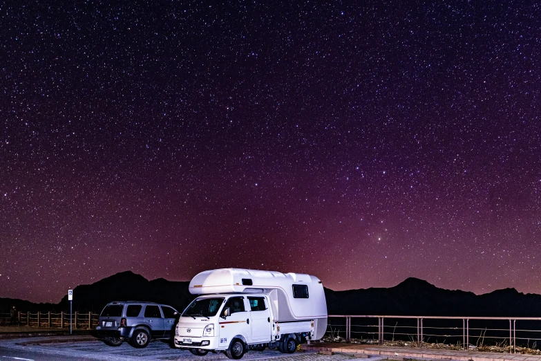 two recreational vehicles parked next to a fence under stars