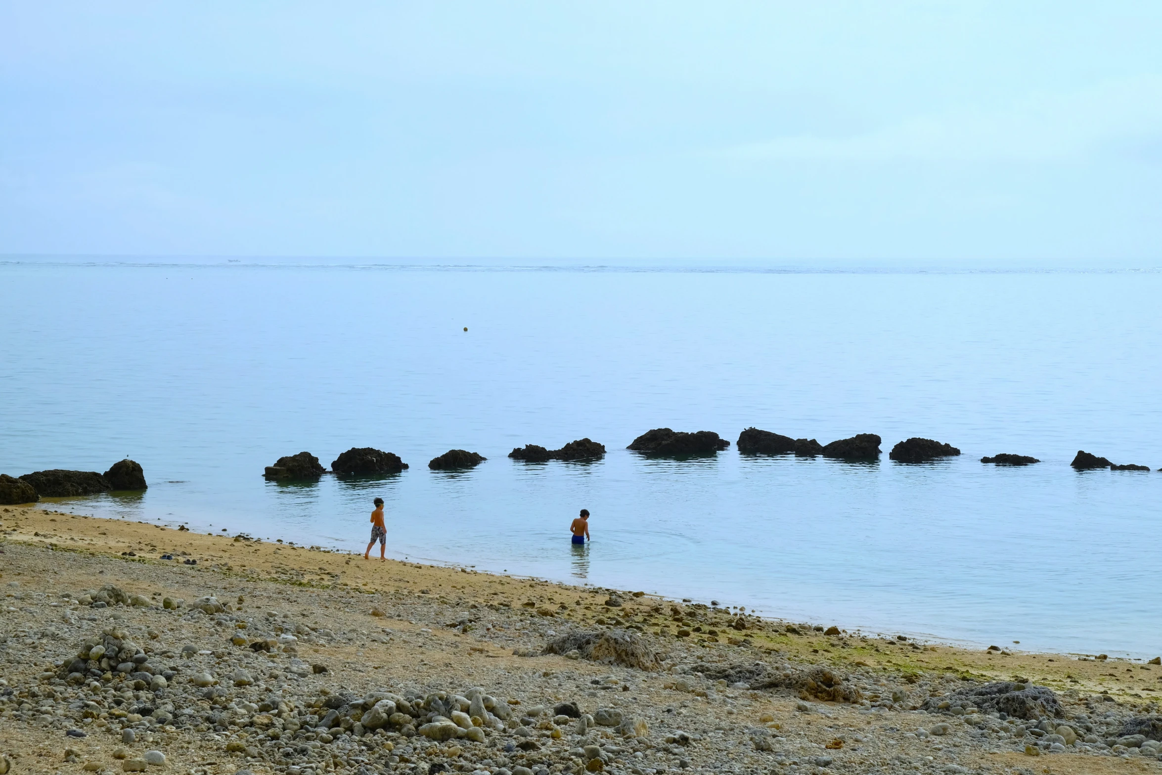 two people stand at the edge of a lake near boulders