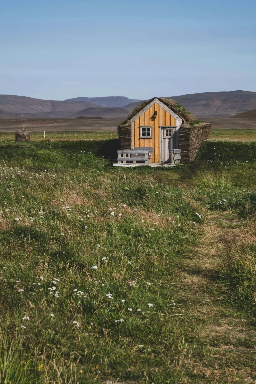 a building in the middle of a field with hills behind