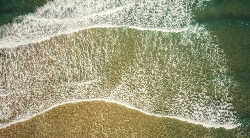 an aerial view of a shoreline with green waves and a sandy beach