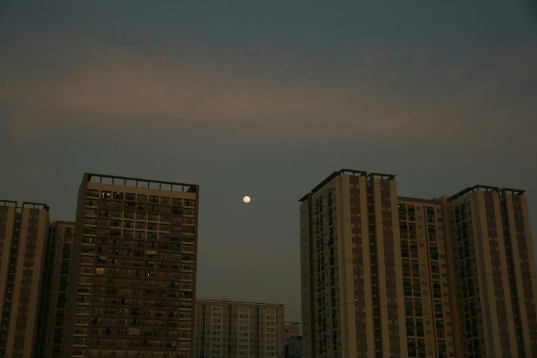 a moon rising over tall buildings, with the lights on