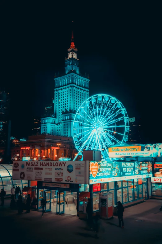 a lit up ferris wheel in the city with buildings