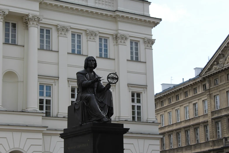 statue with globe in hand in front of large building
