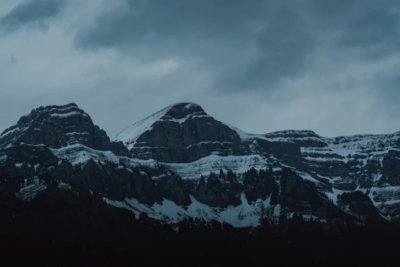 the mountain top is covered in snow as clouds loom in front