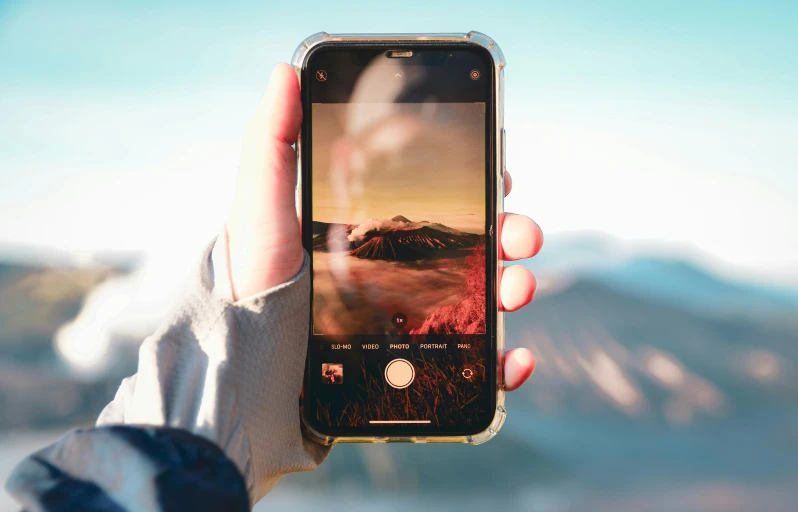 someone holds an apple iphone and pographs a landscape