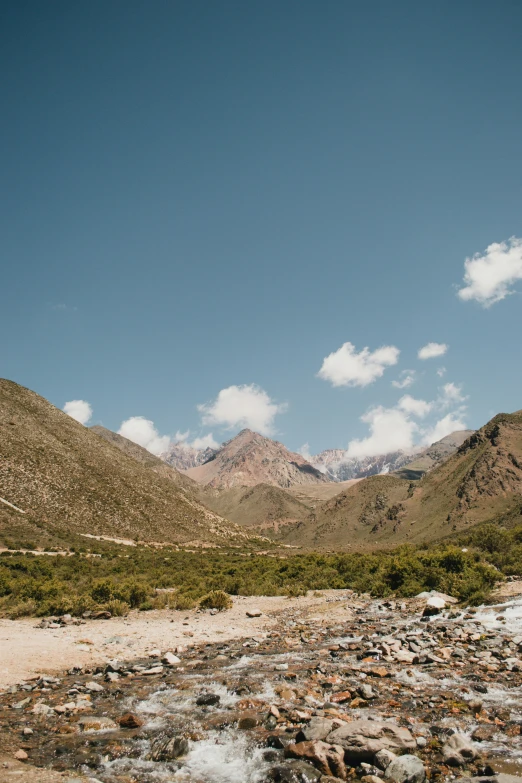 a mountain side with rocks and plants below and blue sky