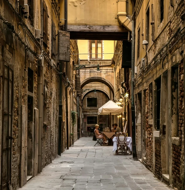 a narrow walkway in the city with tables and umbrellas