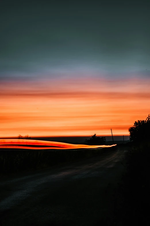 a dark country road with a red, orange and blue sky